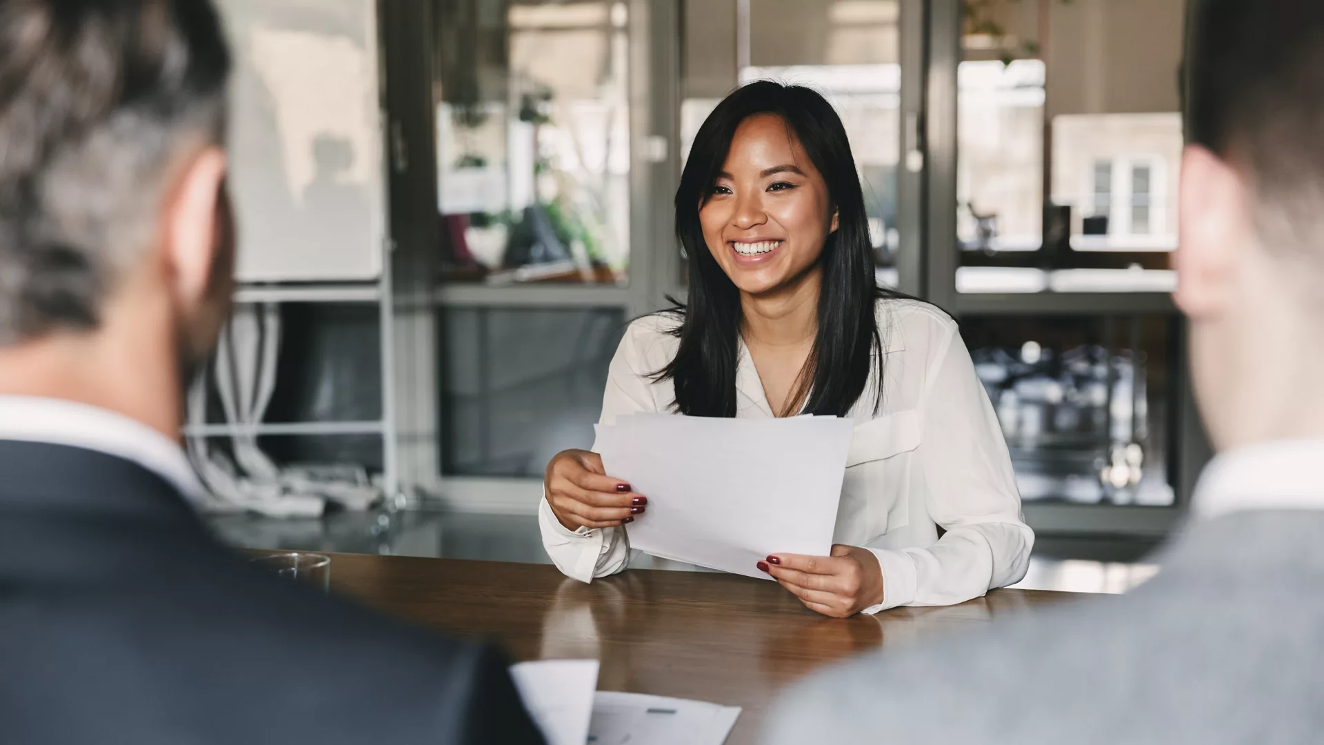 Business, career and placement concept - young asian woman smiling and holding resume, while sitting in front of directors during corporate meeting or job interview